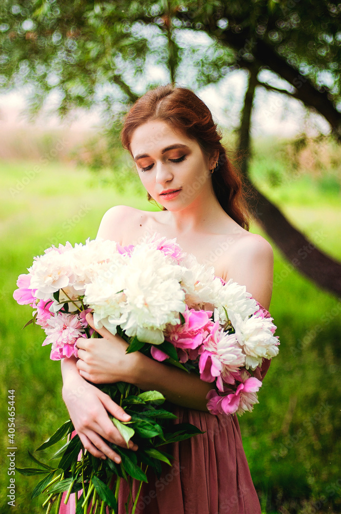 Fototapeta premium Outdoor portrait of young redhead woman in nature with big bouquet of pink peonies. Woman's Day. Female spring, summer fashion concept.