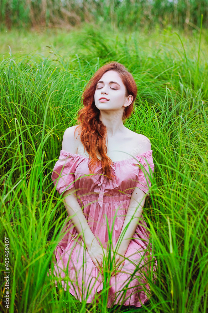 Outdoor portrait of young redhead woman in field of green grass with pink peony. Woman's Day. Female spring, summer fashion concept. Outdoor portrait of young redhead woman in field of green grass with pink peony. Woman's Day. Female spring, summer fashion concept.