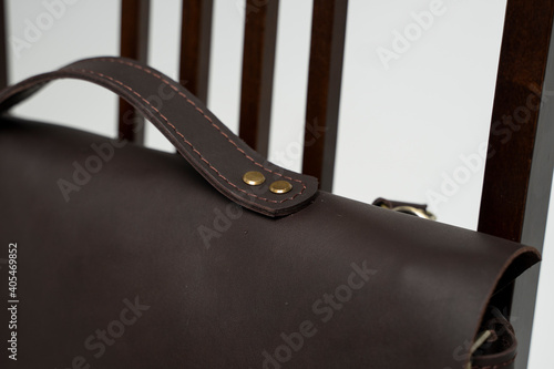 Details of brown men's shoulder leather bag for a documents and laptop on a brown chair with a white background. Mens leather brief case, messenger bags, leather satchel, handmade briefcase.