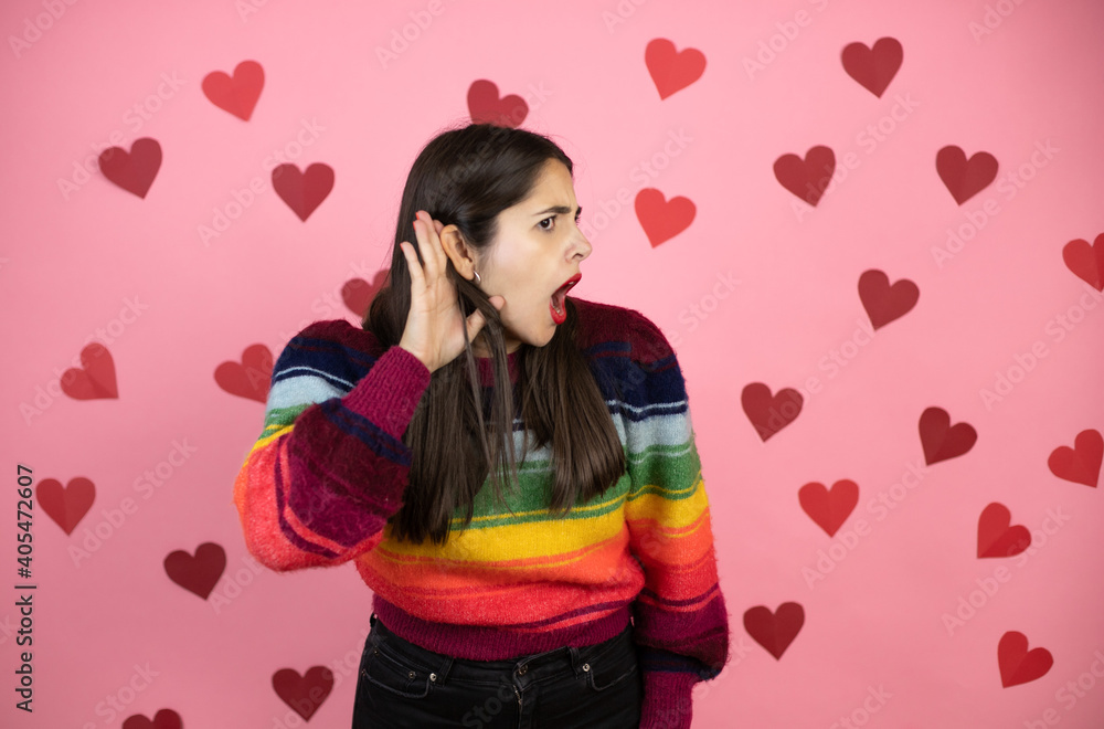 Young beautiful woman over pink background with harts surprised with hand over ear listening an hearing to rumor or gossip Young beautiful woman over pink background with harts surprised with hand over ear listening an hearing to rumor or gossip