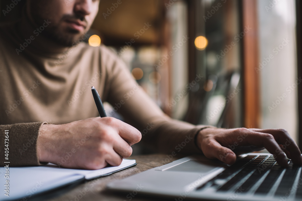 Crop man working on laptop and taking notes in notebook Crop man working on laptop and taking notes in notebook