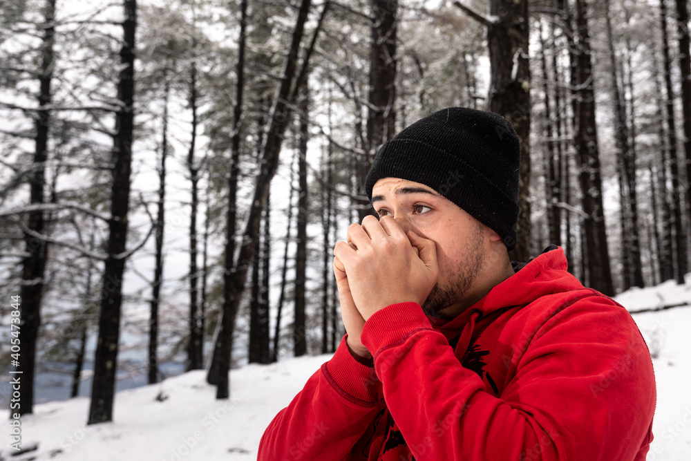 Young man trying to warm his hands on a snowy forest Young man trying to warm his hands on a snowy forest