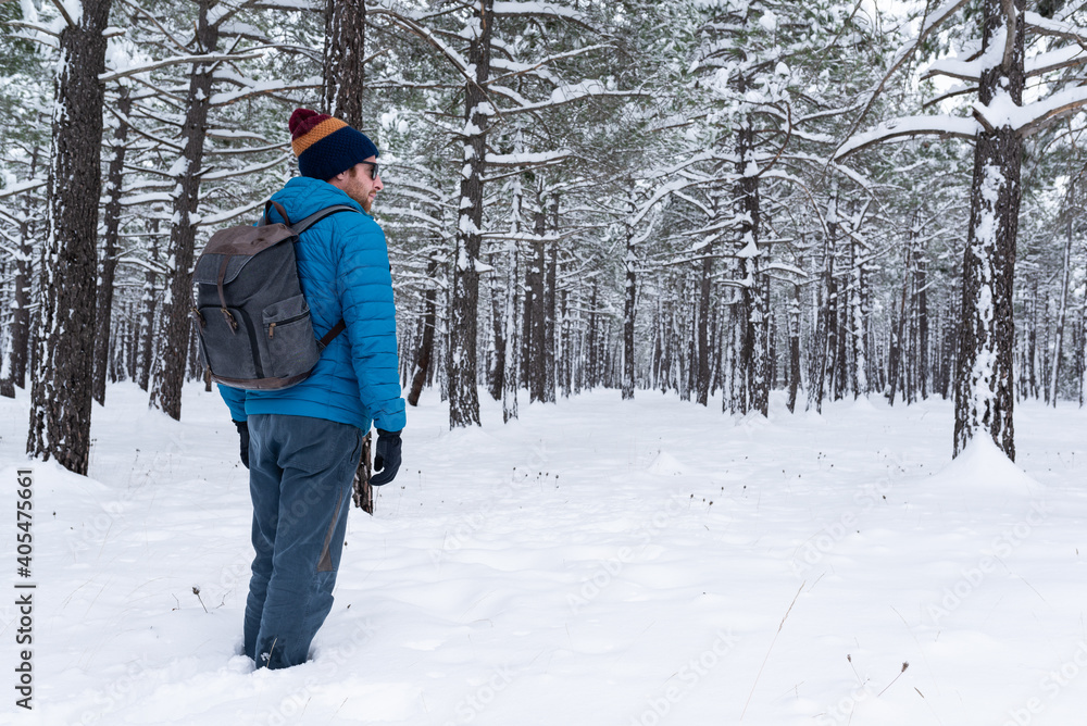 Side view of a young man practising trekking on a beautiful snowy forest. 