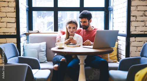 Fotografija Young couple spending time in restaurant while watching photos on smartphone