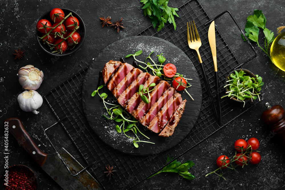 Cooked juicy tuna steak with vegetables on a black stone plate. Restaurant food. Seafood. Rustic style. Flat Lay. Cooked juicy tuna steak with vegetables on a black stone plate. Restaurant food. Seafood. Rustic style. Flat Lay.