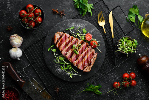 Foto Cooked juicy tuna steak with vegetables on a black stone plate