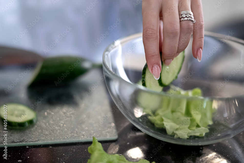 Process of preparing a vegetable salad, shifting cucumber slices into glass bowl. Healthy vegan eating and lifestyle Process of preparing a vegetable salad, shifting cucumber slices into glass bowl. Healthy vegan eating and lifestyle