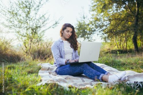 Beautiful woman, resting sitting onthe grass, and using a laptop