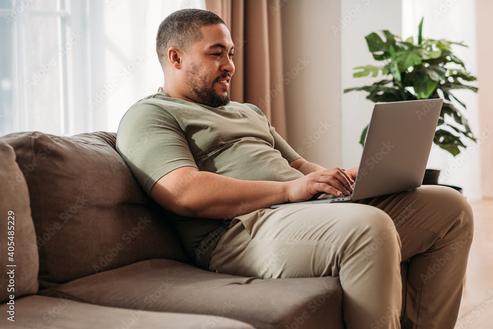 Smiling man with laptop on his hips sitting on a sofa. Young male working from home. Smiling man with laptop on his hips sitting on a sofa. Young male working from home.