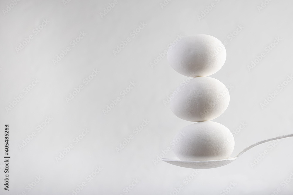 three white ceramic eggs stacked in balance on a white spoon against white background. Food concept. Copy Space three white ceramic eggs stacked in balance on a white spoon against white background. Food concept. Copy Space