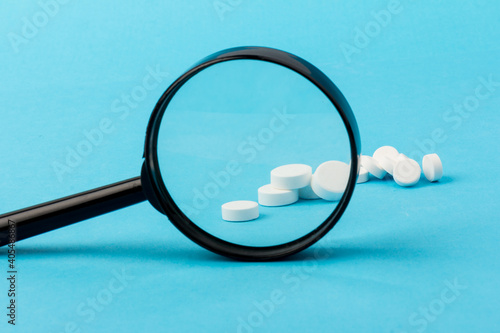 Concept - pharmaceutical testing, testing of medicines, magnifying glass, tablets on a blue background. Doping control.