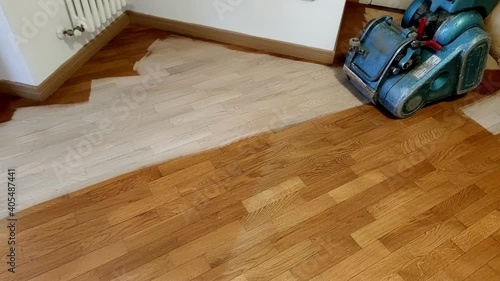 Worker man sanding wooden floor of parquet, with pad sander machine in an empty room during a renovation. Sand and refinish hardwood floors.