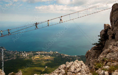 Against the background of the city and the blue sea at a great height, tourists walk over the abyss on rope bridges. Experience the thrill. Mount Aypetri, Yalta, Crimea.