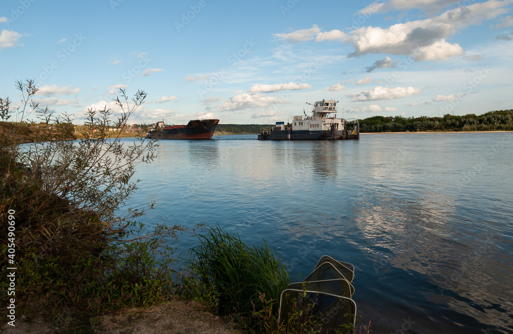 Tugboats are hauling an old barge for scrap. A large river, blue sky and clouds are reflected in the calm water. Oka River, Ryazan region, Russia.