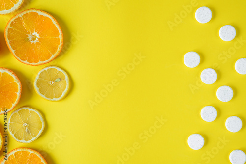 Top view of Fruits and white pills in front of each other on the yellow background, concept of fruits against synthetic vitamins, free space for text in the middle