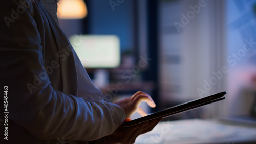 Close-up photo of woman hands typing on tablet checking financial graphs standing in start-up office late at night. Businesswoman using social network, texting and blogging working overtime for job