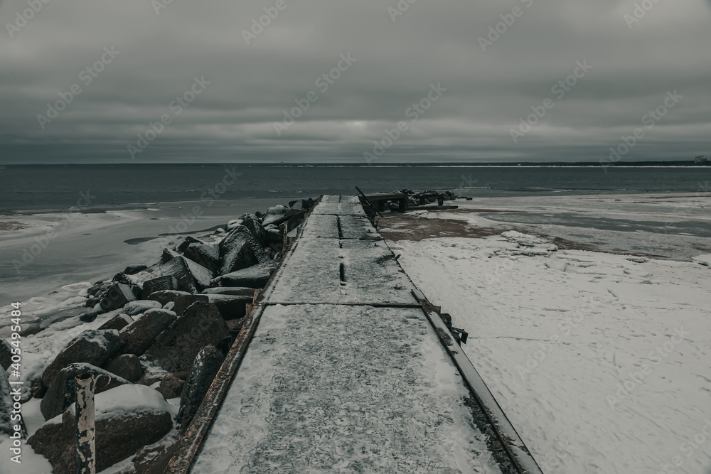 The stone pier goes into the frozen sea. Cold winter evening. Cloudy weather. Snowy day.

