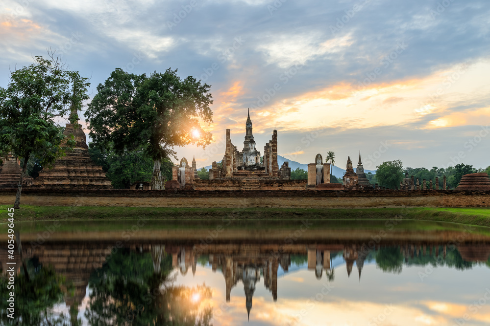 Buddha statue and pagoda Wat Mahathat temple with reflection during sun set, Sukhothai Historical Park, Thailand