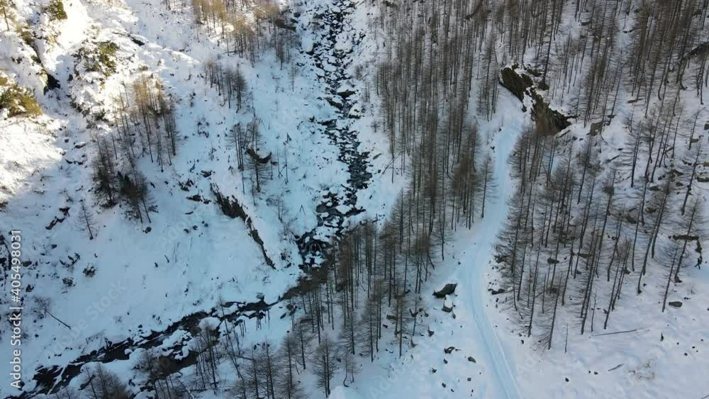 Drone flight over the snowy mountains. Water flowing into the small river, sunny day. Alps, Italy Drone flight over the snowy mountains. Water flowing into the small river, sunny day. Alps, Italy