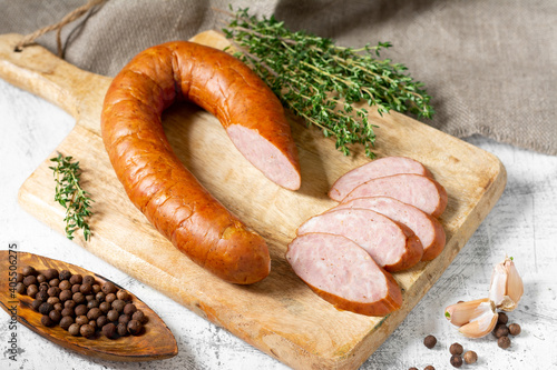 Smoked Cracow sausage on a wooden serving board on a light gray kitchen table. Slicing boiled and smoked sausage 