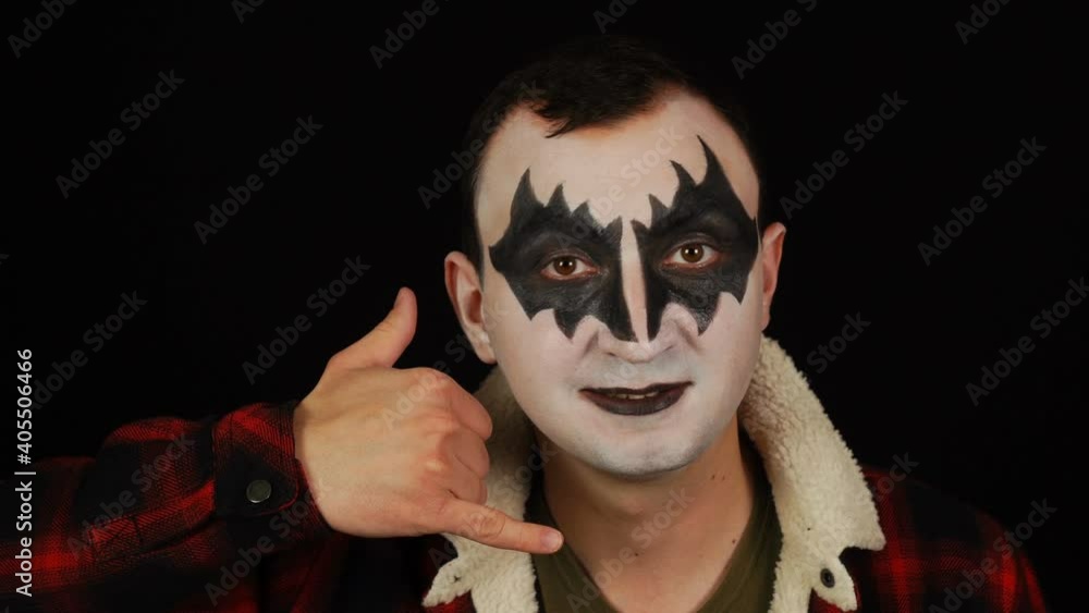 Man in demon makeup making call me gesture to camera on black background Man in demon makeup making call me gesture to camera on black background