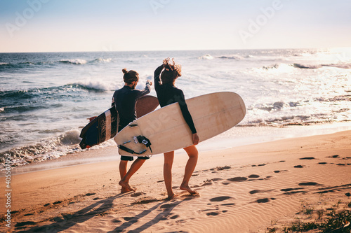 Canvas Print Young beautiful couple walking along the sandy beach near the ocean at sunset wi