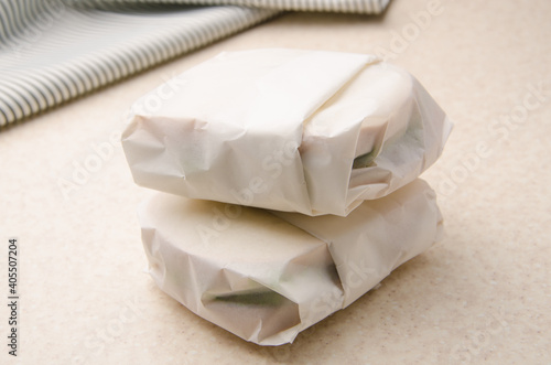 Two sandwiches wrapped in parchment paper on kitchen table