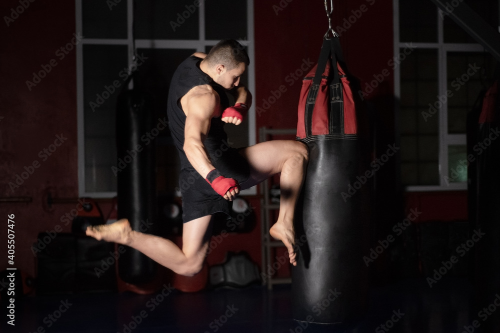 Kickboxing fighter Performing Jumping Air Kicks with Knee on Punch Bag. Caucasian Man Practicing Martial Arts Training at Urban Gym. High quality photo.