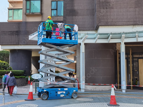 worker with face mask cleans dirts (pigeon excrement or droppings) on glass roof of rain shelter standing on slab scissor lift in a residential building complex in Hong Kong during covid-19 photo