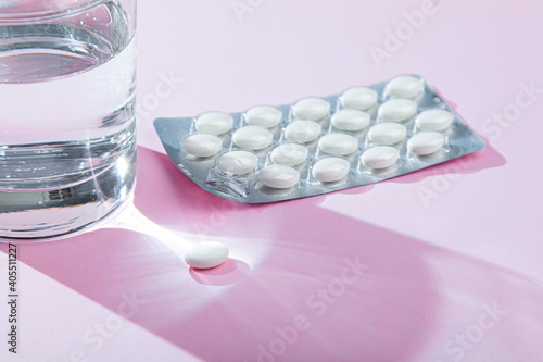 Water glass, blister with medical pills, tablets, vitamins on pink background