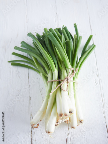 bunch of spring onions tied with string on a white wooden table