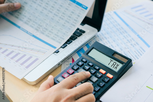 Close up Businessman and partner using calculator and laptop for calculating finance, tax, accounting, statistics, and analytic research concept. Tax word on a calculator. Business and tax concept.