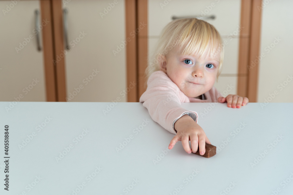 Little blonde girl reaches for chocolate candy lying on the table Little blonde girl reaches for chocolate candy lying on the table