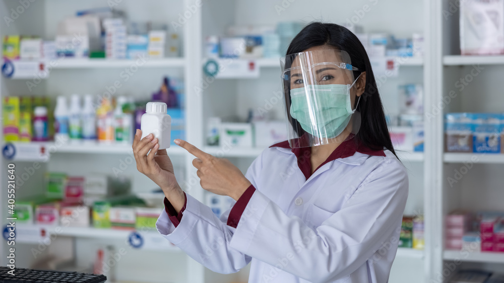 Asian Professional women pharmacist with protective face shield on his face working in modern drugstore and showing white medicine bottle in hand at pharmacy store Thailand Asian Professional women pharmacist with protective face shield on his face working in modern drugstore and showing white medicine bottle in hand at pharmacy store Thailand