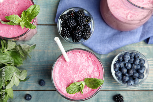 Fototapeta Naklejka Na Ścianę i Meble -  Tasty fresh milk shakes with berries on light blue wooden table, flat lay