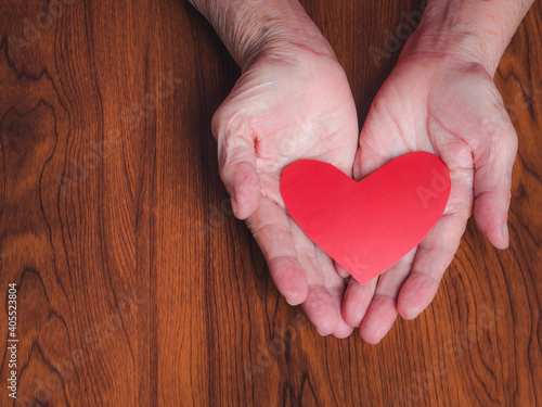 Red paper cut a heart shape on the palm of a senior woman. Valentine's day. Close-up photo. Concept of aged people and love