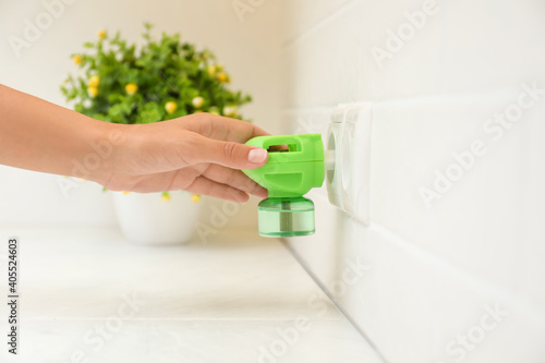 Φωτογραφία Woman plugging electric vaporizer with insect repellent liquid at home, closeup
