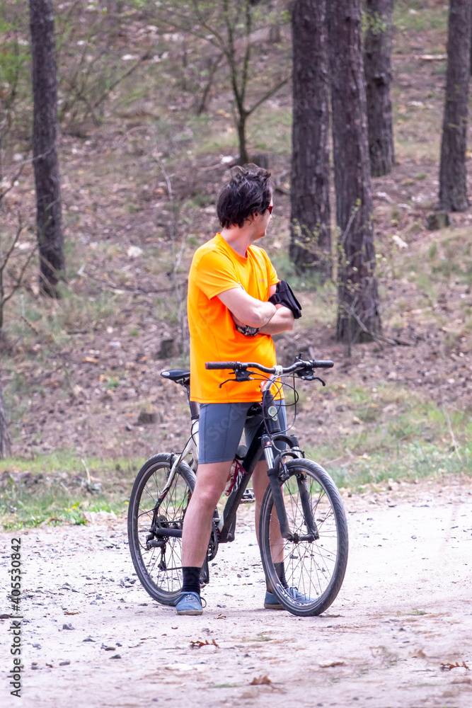 man with a bicycle in the forest stands on the trail and waits for the others, after the arrival, vertical