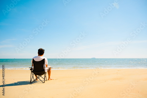 Man sitting on black chair on the beach with sea in background