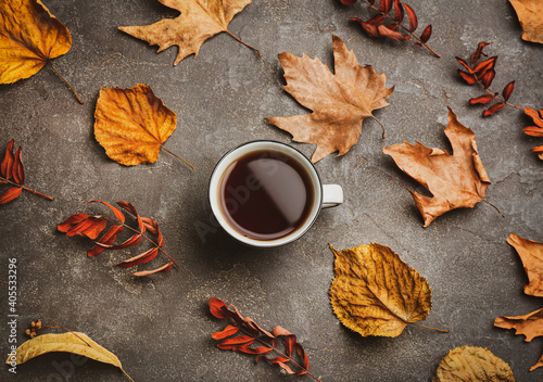 Cup of hot drink and autumn leaves on grey table, flat lay. Cozy atmosphere
