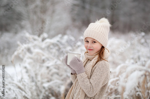Cute baby girl smiling and holding a mug of hot drink tea outdoors in winter park. Winter time concept