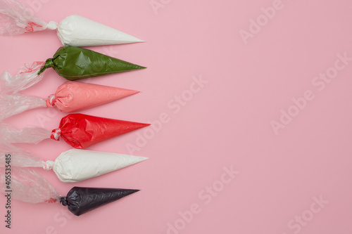 Multicolored glazing in icing bags on a pink background.  Set for decorating desserts.  Icing for gingerbread, brownies and cakes in pastry bags. Cake decorating tools. photo
