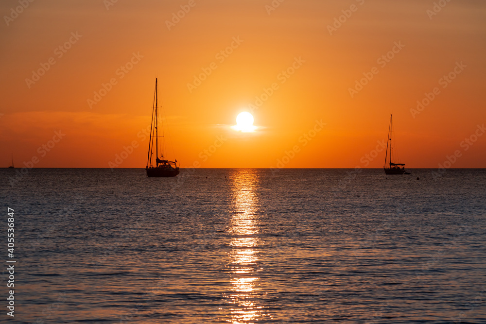 Two sailboats sailing across the ocean against a golden sunset