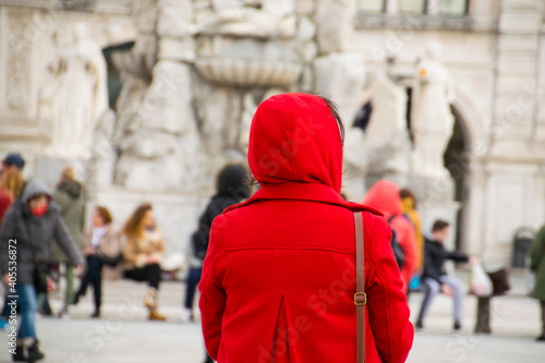 Persona di spalle con giubbotto rosso in piazza con sfondo sfocato, persone sullo sfondo