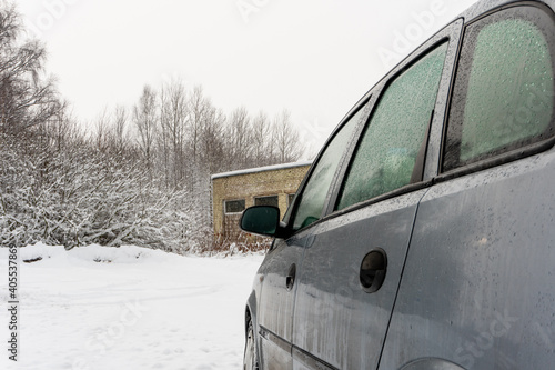 Dirty car on the background of an abandoned building and bushes on a snowy road, car breakdown on the road © Oleg