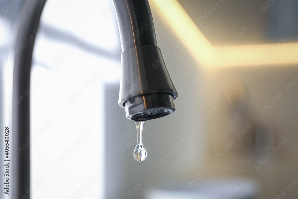 Water drop falling down from tap on blurred background, closeup Water drop falling down from tap on blurred background, closeup