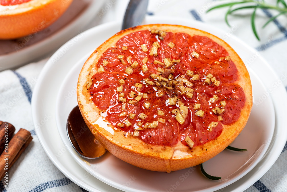 Sweet baked grapefruit with honey, cinnamon, and ginger in a white plate on a served table close-up. Sweet baked grapefruit with honey, cinnamon, and ginger in a white plate on a served table close-up.