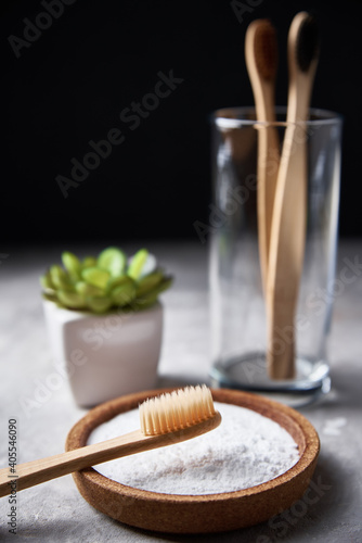 Bamboo toothbrushes in glass, baking soda and bathroom towels on dark background