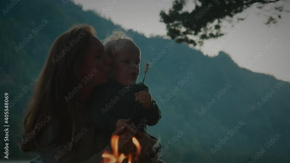 Mom and baby son fry marshmallows on a campfire in the open air late at night. Mom and son blow