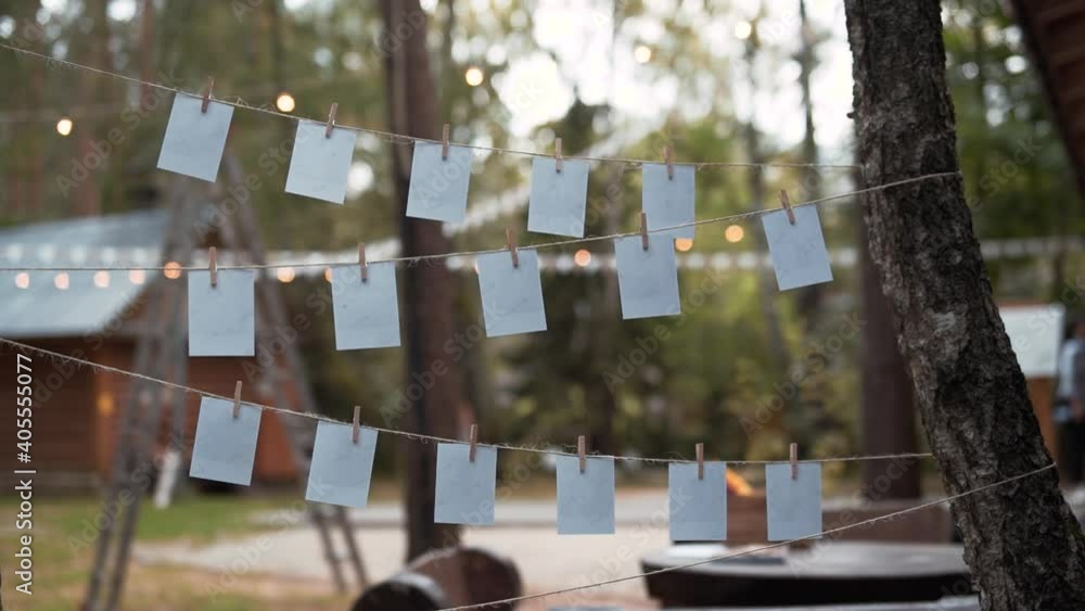 White sheets of paper are hanging on a rope on wooden clothespins, the string is stretched between tree trunks. In the background there is a house, stairs, flags and green trees. White sheets of paper are hanging on a rope on wooden clothespins, the string is stretched between tree trunks. In the background there is a house, stairs, flags and green trees.